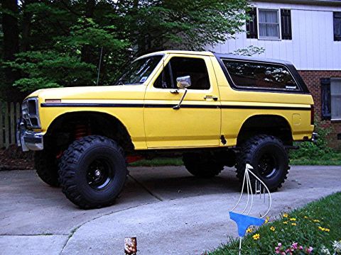 1985 Ford Bronco - Lifted yellow Ford Bronco with large tires sits on a paved driveway.
