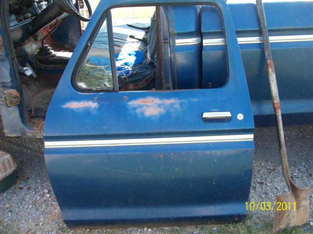 blue pickup truck door open, showing interior with worn seats and steering wheel. A shovel leans against the truck bed