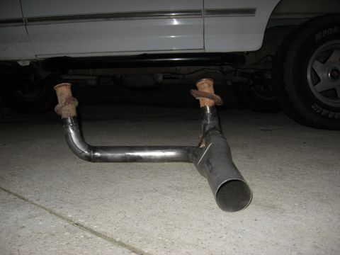 1994 Ford Bronco - A custom exhaust system is laid out on the ground next to a vehicle's undercarriage.