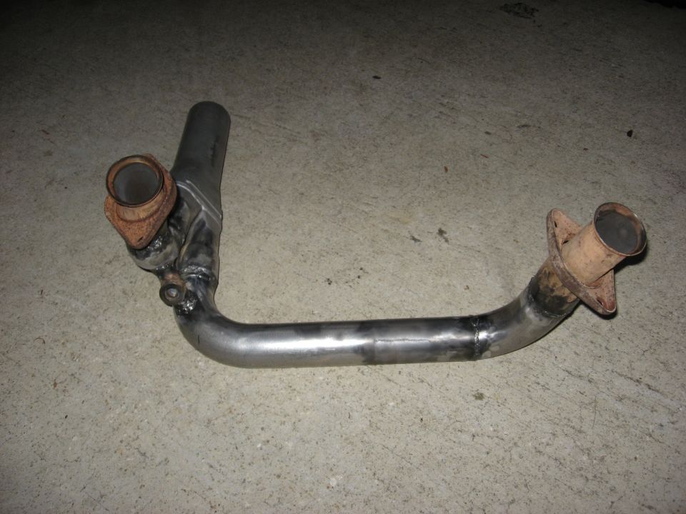 Exhaust pipe with two flanges, one rusted, welded together and resting on concrete