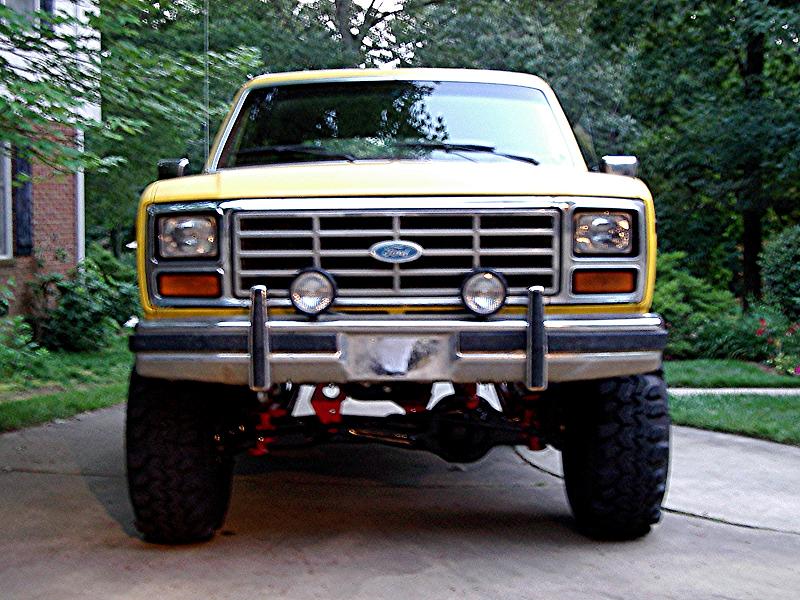 Front view of lifted yellow Ford Bronco with chrome grille and round driving lights