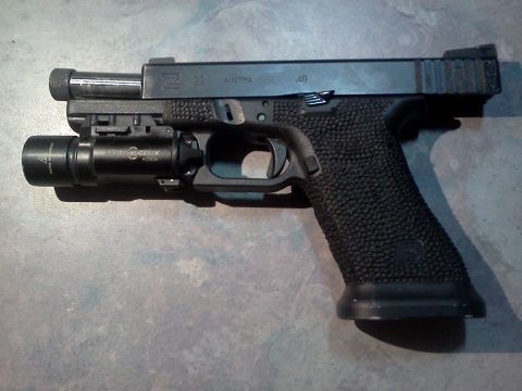1996 Ford Bronco - A Glock pistol with a tactical light mounted to the accessory rail sits on a textured surface.