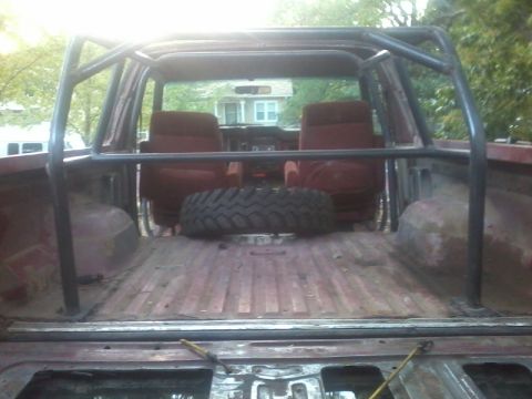 1986 Ford Bronco - The interior of a 1986 Ford Bronco is visible, a roll cage and a spare tire in the cargo area.