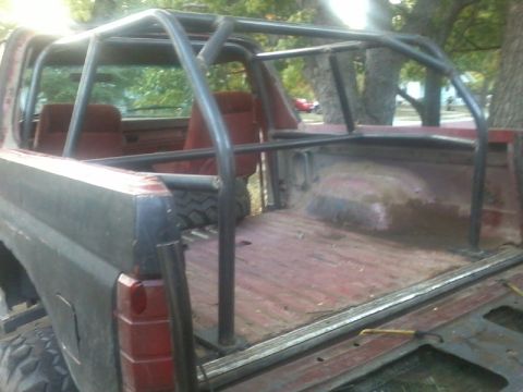 1986 Ford Bronco - This modified Ford Bronco features a custom roll cage and a red interior, seen from a rear angle.