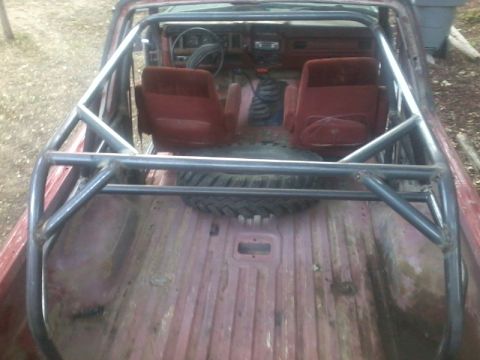 1986 Ford Bronco - View of the interior of a red SUV, a roll cage and a spare tire mounted in the cargo area.