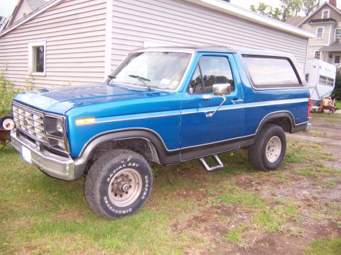 1983 Ford Bronco - A blue two-door Ford Bronco full-size SUV with a white hardtop roof, chrome grille and bumper, and Cooper Discoverer Radial AST tires on si…