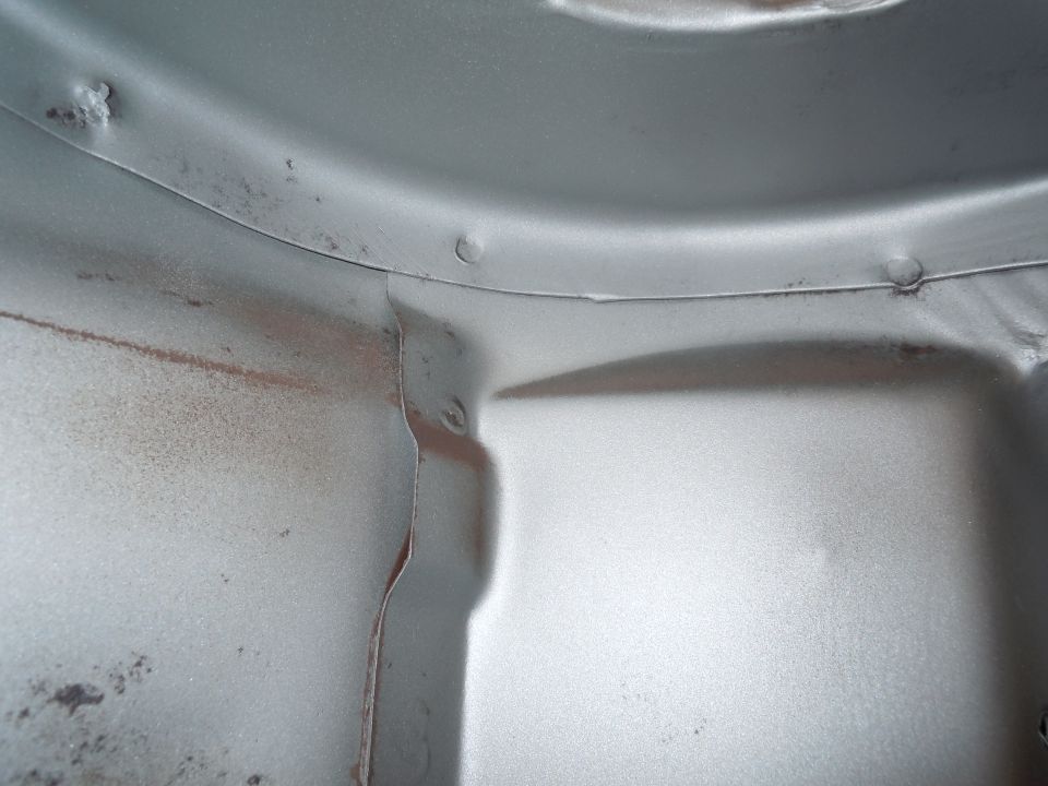 Close-up of the underside of a car, showing metal panels and some rust spots. Supermotors.net logo visible