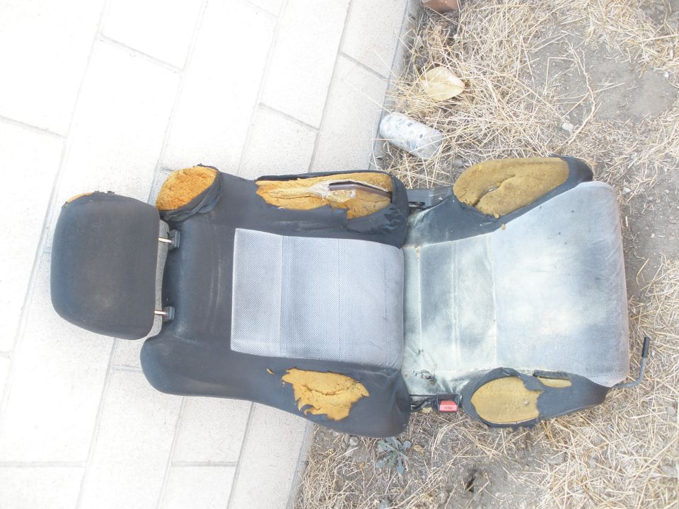 Worn cloth and vinyl car seat lying on pavement with torn foam exposed