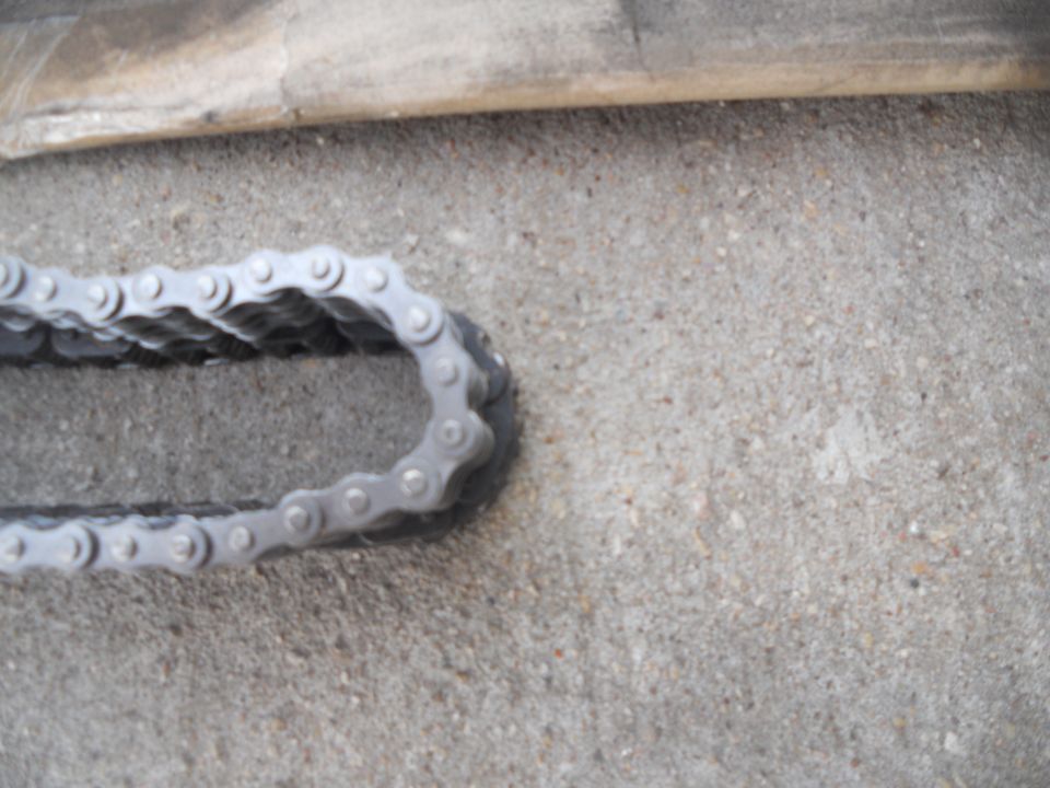 Close-up of a metal chain on a concrete surface. Supermotors.net logo visible