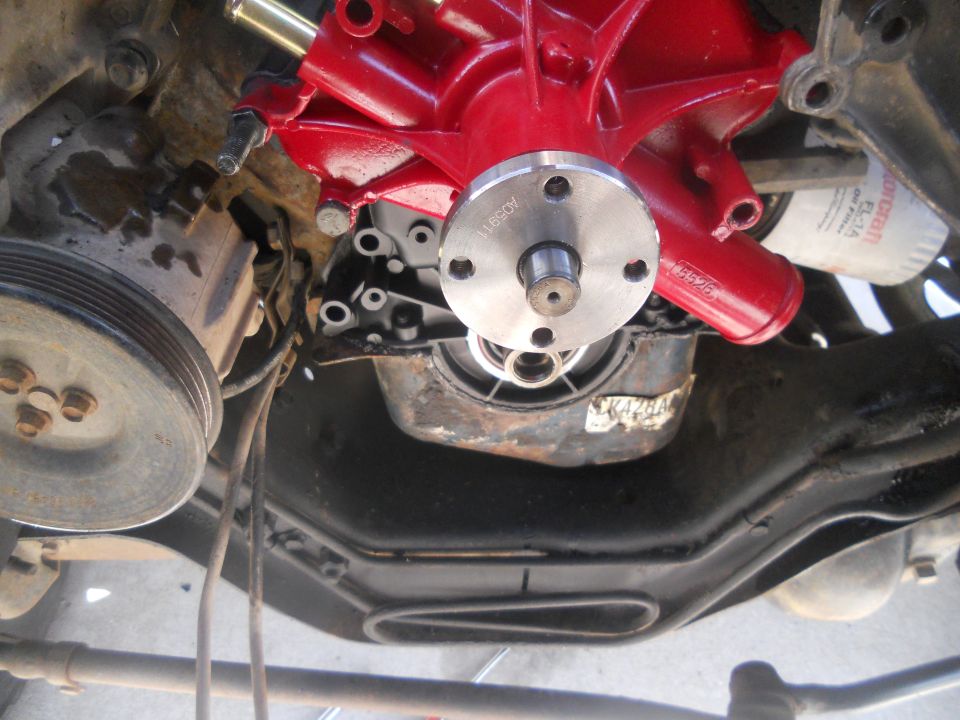 Red engine water pump assembly attached to engine block with metal pulley visible
