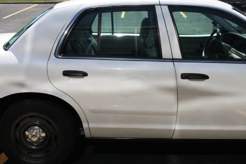 2003 Ford Crown Victoria - The side profile of a white 2003 Ford Crown Victoria sedan is visible, with a focus on the rear passenger door and wheel.