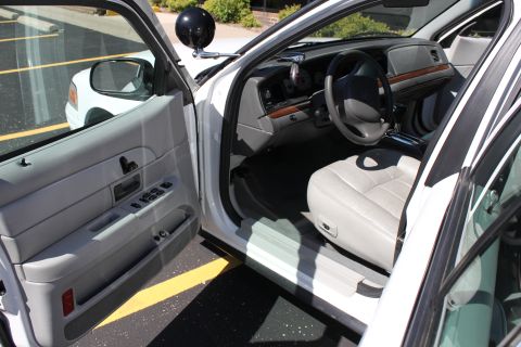 2003 Ford Crown Victoria - The interior of a white sedan is shown, with a view of the driver's seat and dashboard. Another vehicle is parked nearby.