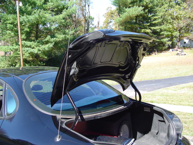 Black sedan with trunk lid raised showing painted lid underside and subwoofer box