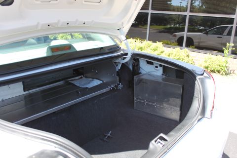 2003 Ford Crown Victoria - The trunk of a white 2003 Ford Crown Victoria shows custom metal storage compartments and a document inside.