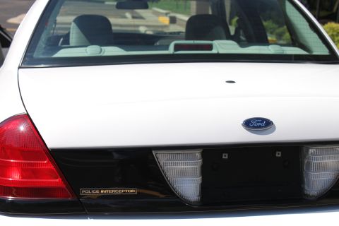 2003 Ford Crown Victoria - Rear view of a white Ford Crown Victoria Police Interceptor sedan, showing the Ford badge and 'Police Interceptor' emblem.