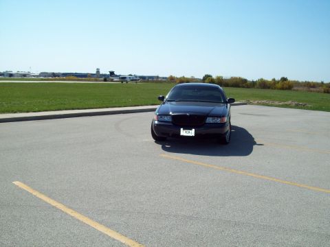 1999 Mercury Grand Marquis - A black 1999 Mercury Grand Marquis is parked on an asphalt lot with an airplane visible in the distance.