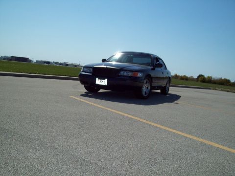 1999 Mercury Grand Marquis - A dark sedan is parked on an asphalt lot under a clear blue sky.