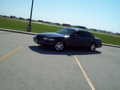 1999 Mercury Grand Marquis - A dark sedan is parked in a lot under a clear blue sky.