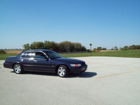 1999 Mercury Grand Marquis - Dark blue sedan parked on asphalt lot under a clear blue sky.