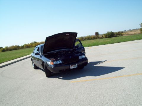 1999 Mercury Grand Marquis - The front of a black sedan is visible with its hood and driver's door open under a clear blue sky.