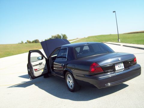 1999 Mercury Grand Marquis - Dark sedan, possibly a 1999 Mercury Grand Marquis, parked with hood and driver door open under a clear sky.