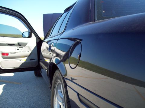 1999 Mercury Grand Marquis - Dark sedan with driver's door ajar and hood raised, seen from the rear passenger side.