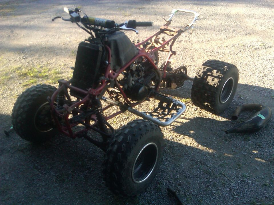 ATV frame with engine, radiator, handlebars, and wheels. Exhaust pipe is detached
