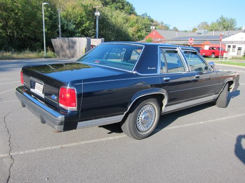 1991 Ford LTD Crown Victoria - A dark blue 1991 Ford Crown Victoria LTD sedan is seen from the 3q-front angle, with a flat front tire visible.