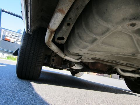 1991 Ford LTD Crown Victoria - Underside view of a car, revealing the fuel tank and exhaust system with the driver's door ajar.