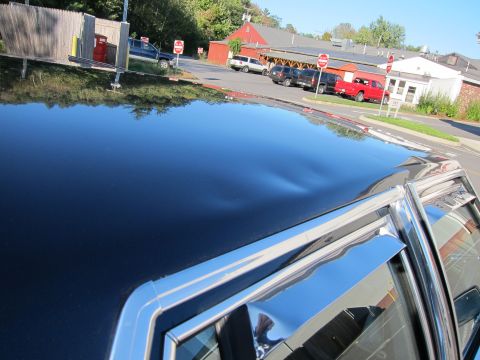 1991 Ford LTD Crown Victoria - A dented black car roof is visible, reflecting a parking lot with several other vehicles and buildings.