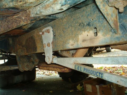 1978 Ford Bronco - Underbody shot looking along the driver-side frame rail of a truck, showing a heavily surface-rusted boxed frame, a bolted-on bracket and t…