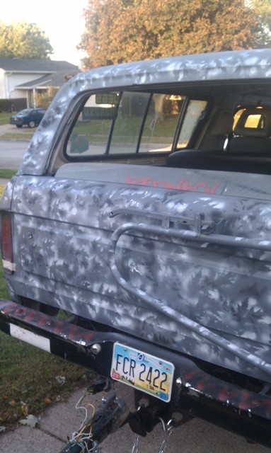 1978 Ford Bronco - The rear of a Ford Bronco, painted in a camouflage pattern, is shown with its license plate visible.