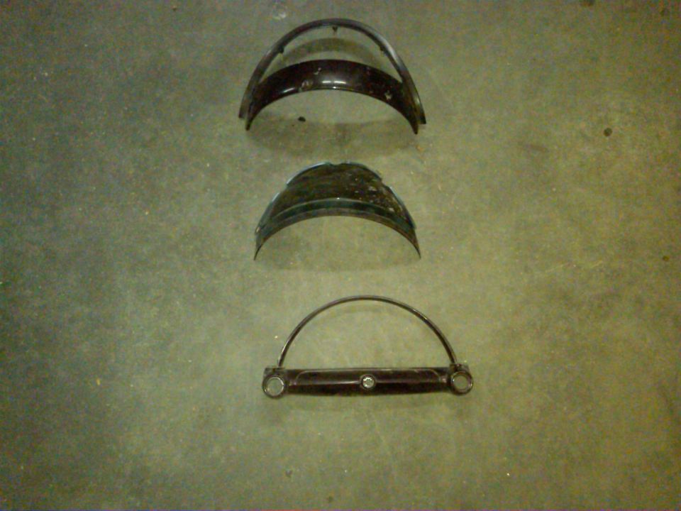 Three curved metal car headlight bezels laid out on a concrete floor