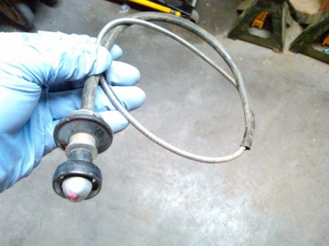 1954 Ford Customline - Throttle cable assembly held by a gloved hand, showing a black knob and metal cable housing.