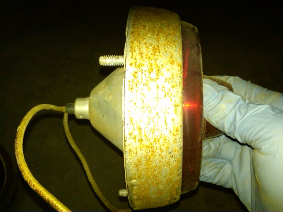 Rusty tail light assembly with red lens and yellow wire, held by a gloved hand