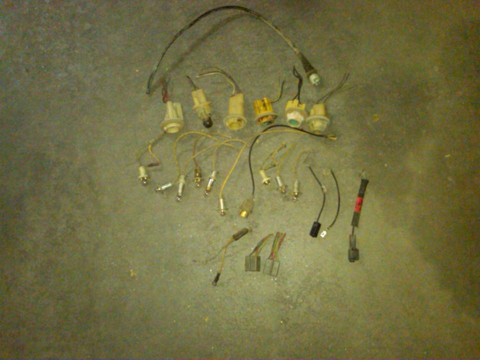 Assorted electrical connectors, bulb sockets, and spark plugs scattered on a concrete floor