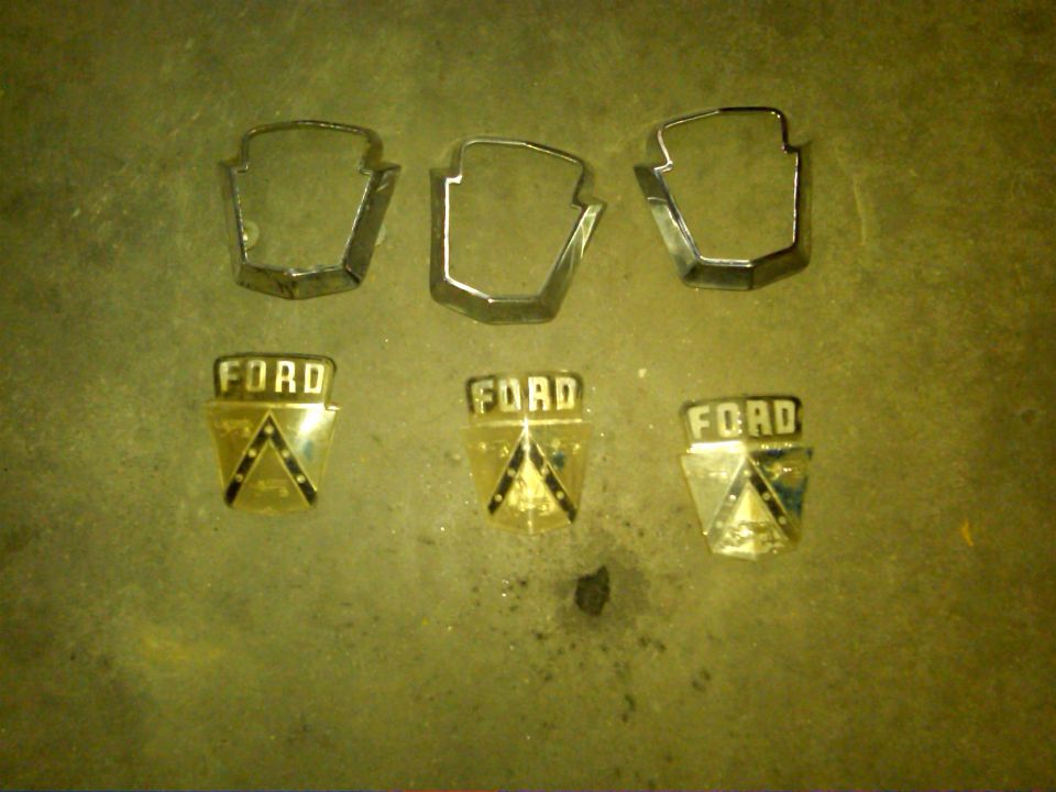 Three 1954 Ford emblems and chrome trim pieces