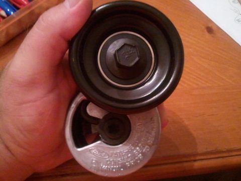 1994 Ford Bronco - A hand holds a pulley and tensioner assembly, identified by a Ford logo and part number F5TE-6B209-BA.