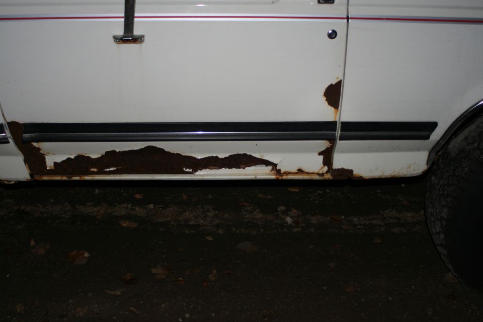 White vehicle's lower door and rocker panel with heavy rust damage and peeling paint