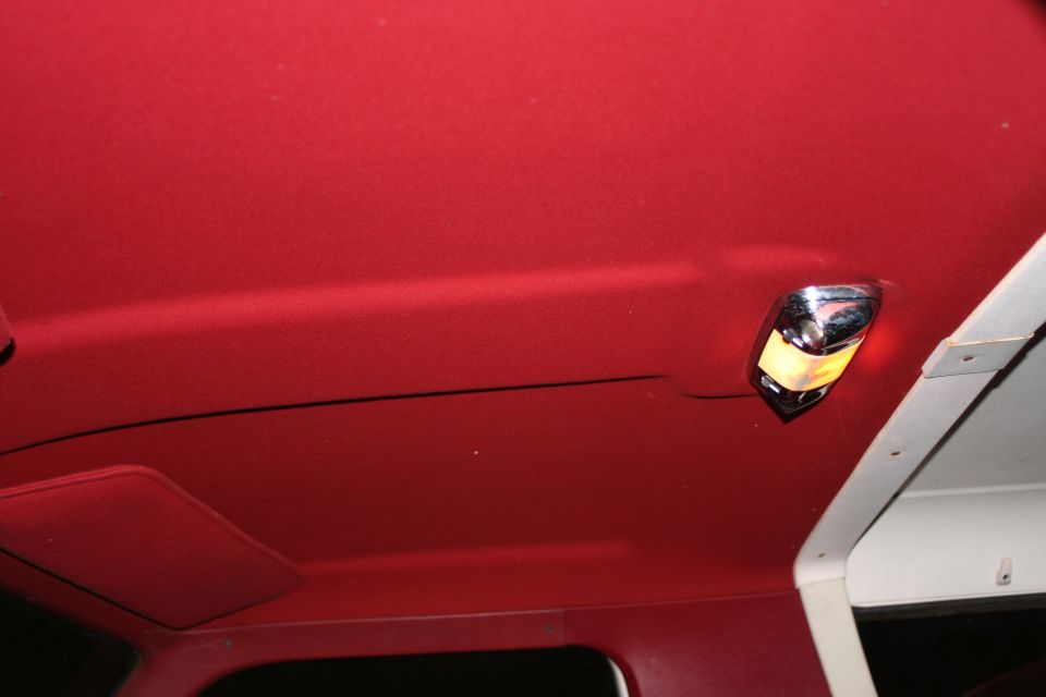 Red headliner inside a Bronco with lit chrome dome light near white rear panel
