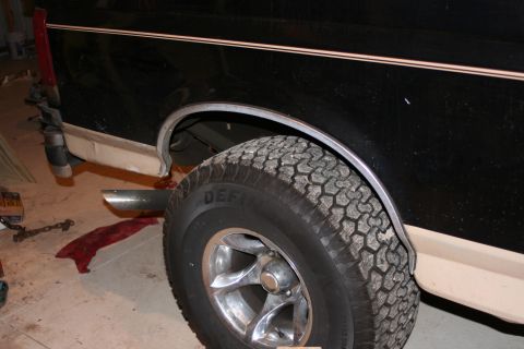 1989 Ford Bronco - Close-up view of the rear wheel well and tire of a two-tone truck, showing the fender and part of the exhaust pipe.