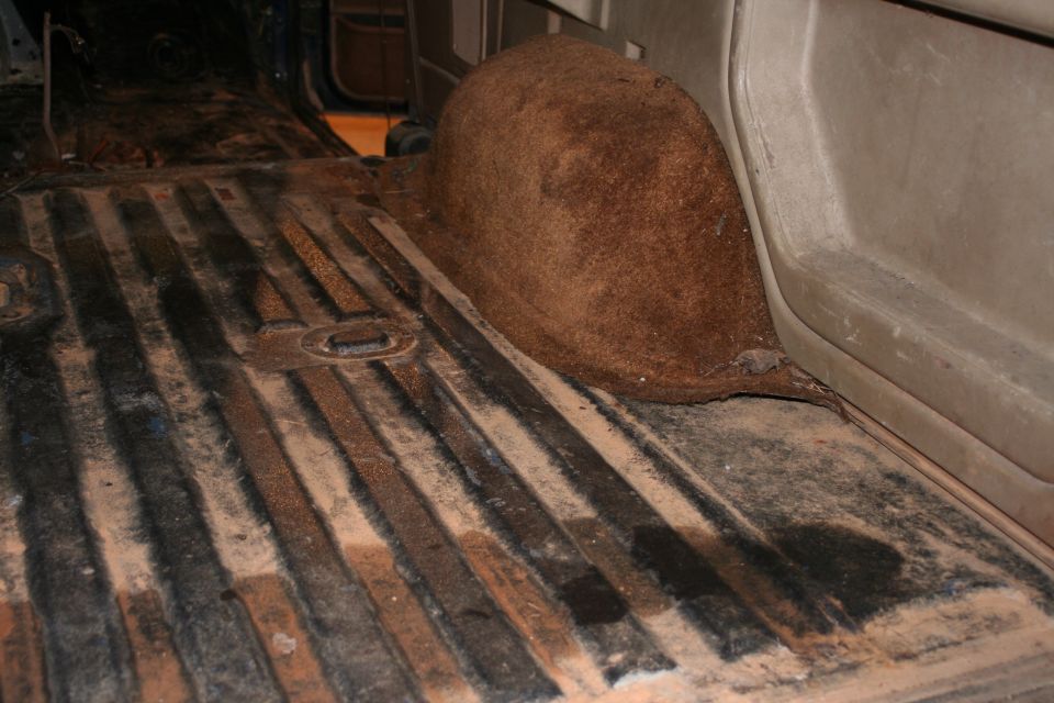 Interior floor and wheel well of a vehicle, showing ribbed metal flooring and brown carpeting