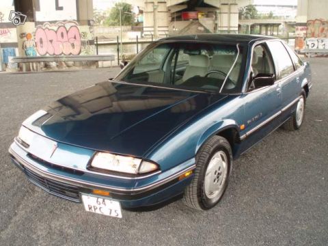 1991 Ford LTD Crown Victoria - A blue sedan is parked outdoors with graffiti on a wall in the background.