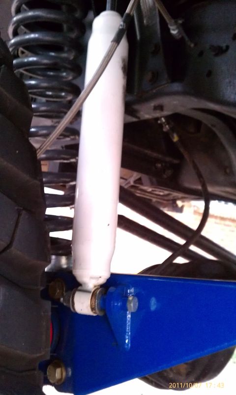 1994 Ford Bronco - Close-up of a white shock absorber and a bright blue suspension arm, part of a vehicle's undercarriage.