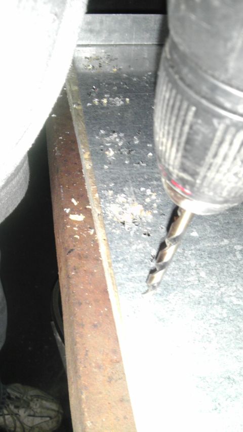 1989 Ford Bronco - Close-up of a drill bit penetrating a metal surface, with visible wood trim and debris.