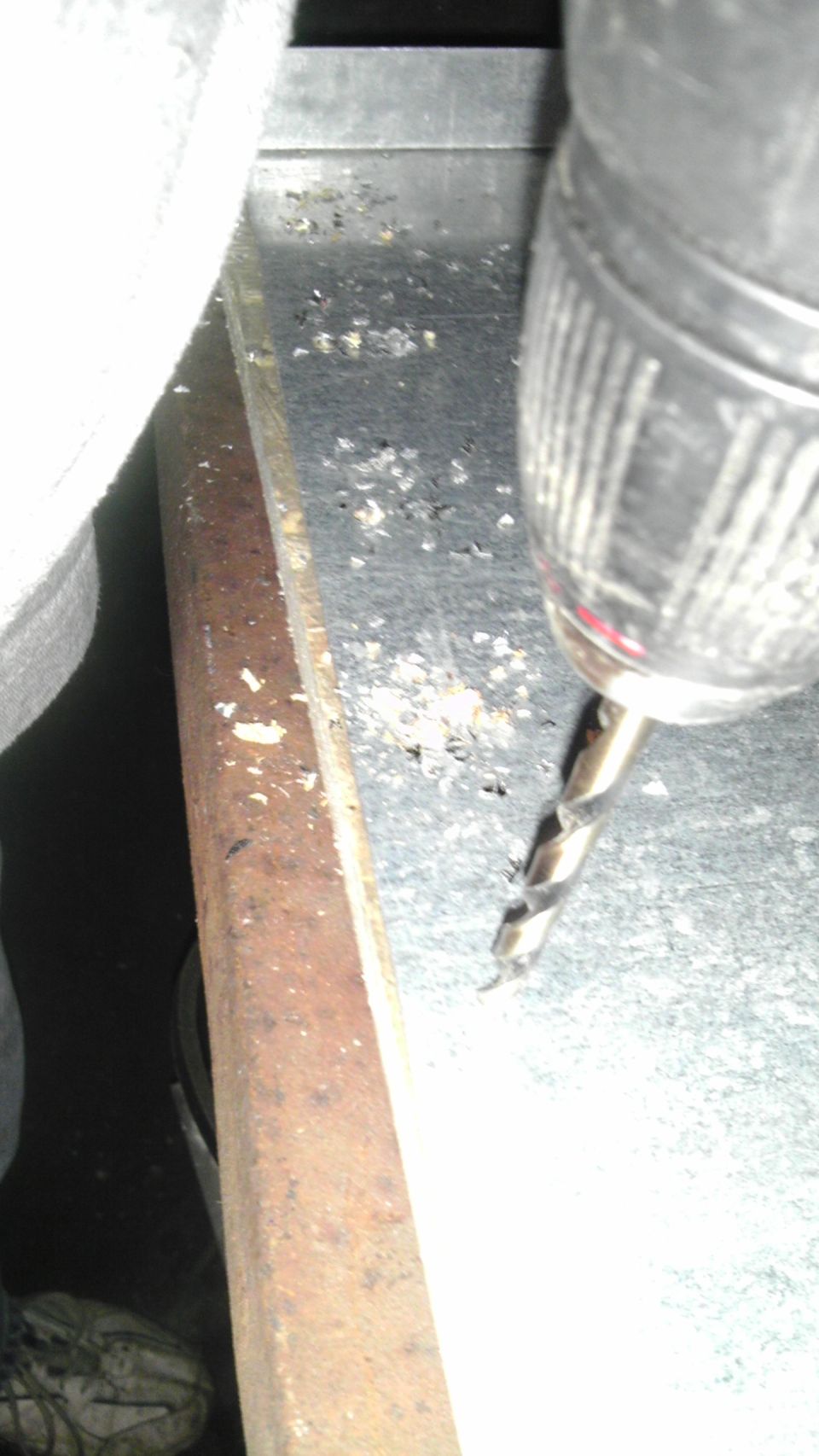Drill bit drilling into a metal surface with wood trim