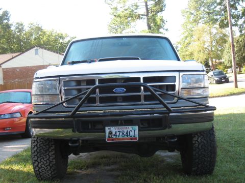 1994 Ford Bronco - Head-on front view of a lifted white Ford SUV with a chrome grille and Ford oval, black tube-style brush guard bolted to the front bumper,…