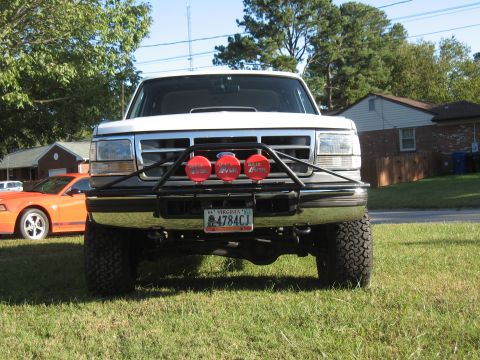 1994 Ford Bronco - 1994 Ford Bronco equipped with a light bar and off-road tires, parked on grass. An orange Ford Mustang is nearby.