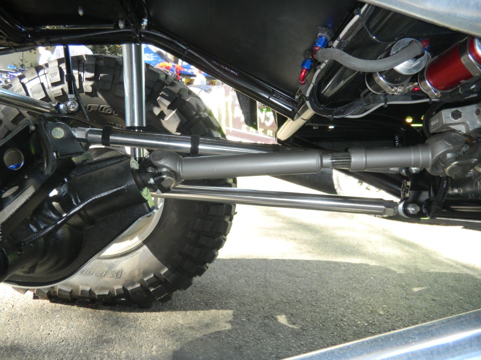 Undercarriage of a modified vehicle with large off-road tires, visible steering components, and suspension parts
