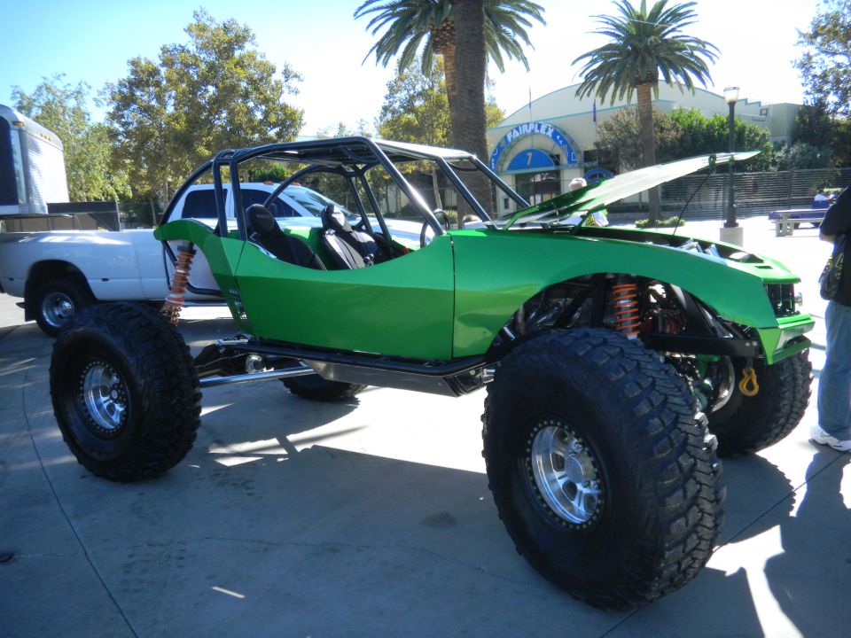 green buggy with big tires, hood open, parked next to a white truck